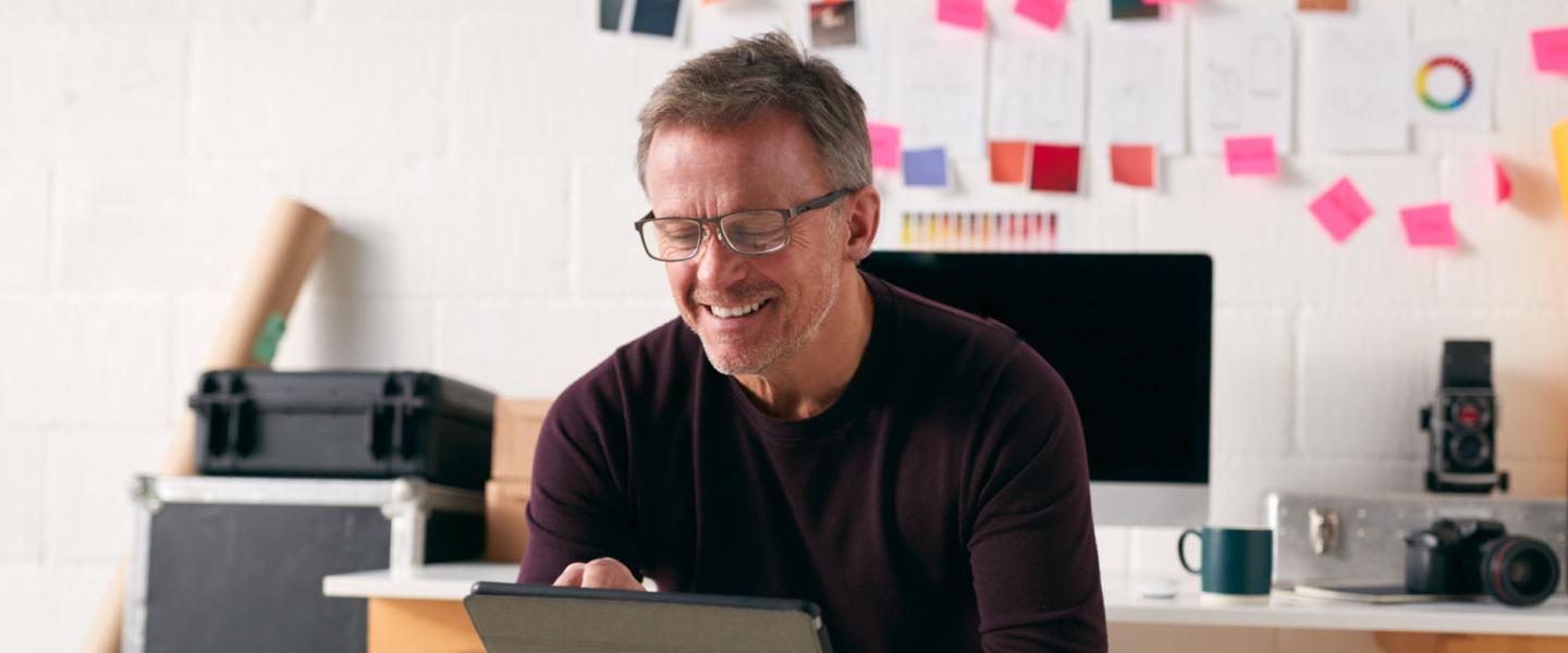 Homme souriant de 60 ans qui prépare sa retraite sur sa tablette